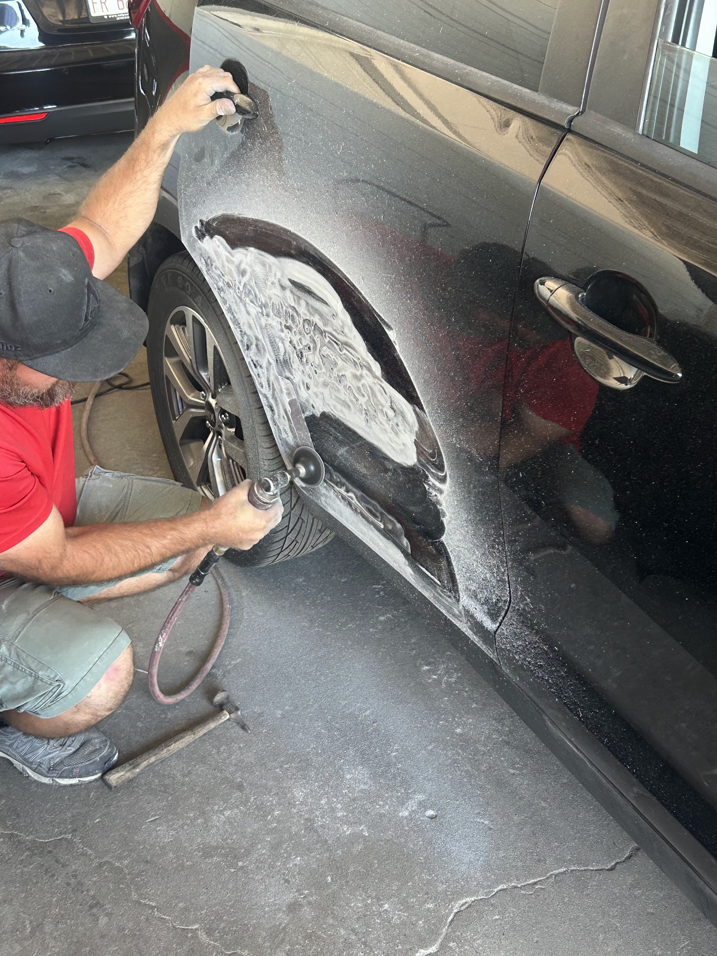 Body shop technician sanding a black car door before repaint — collision repair in Phoenix, AZ